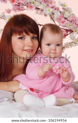 A beautiful mother with her daughter lying in bed on a light background