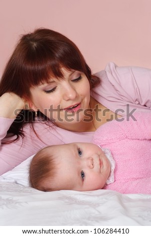 A pretty Caucasian mummy with her daughter lying in bed on a light background