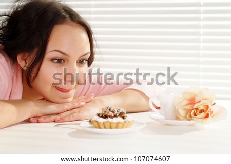 A luck caucasian woman lying at the table with a cake on a light background