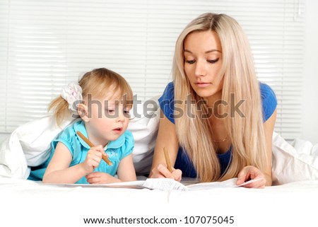 Luck caucasian mother and daughter lying on the bed with a pencils