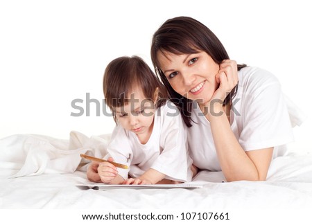 A beautiful Caucasian mummy with her daughter lying on the bed with a pencil