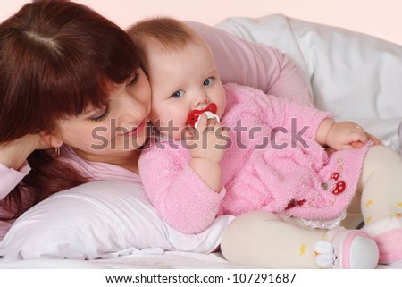 A luck Caucasian mom with her daughter lying in bed on a light background