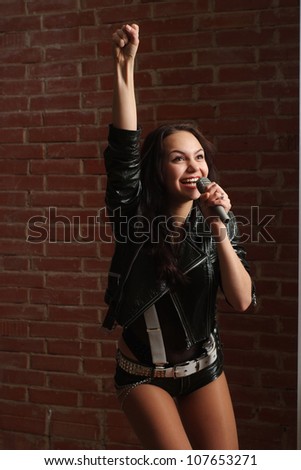 Happy Caucasian female with a microphone singing against a brick wall
