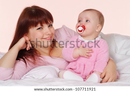A beautiful good mama with her daughter lying in bed on a light background