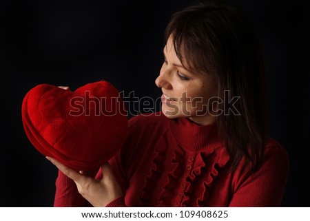 Pretty Caucasian woman with a happy heart pillow on a dark background
