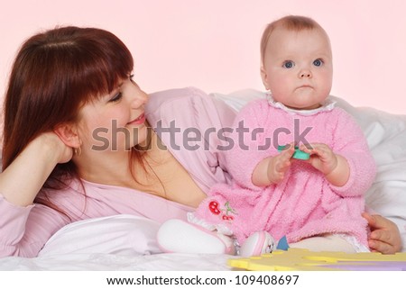 A beautiful nice mother with her daughter lying in bed on a light background