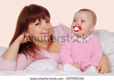 A beautiful mama with her daughter lying in bed on a light background