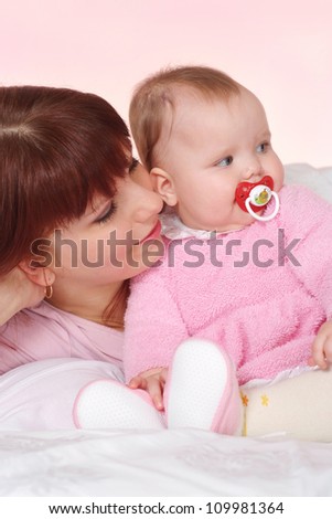 A good Caucasian mama with her daughter lying in bed on a light background