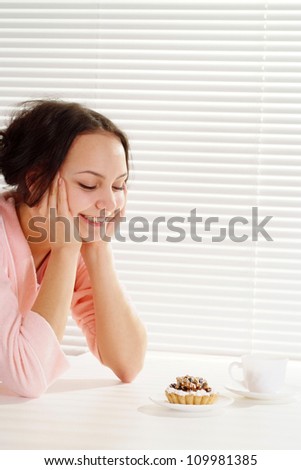 Luck Caucasian lady is and looks at a cake on a light background