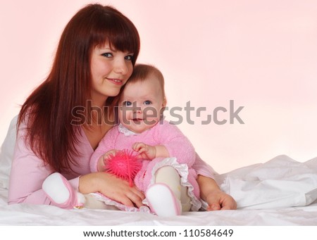 A nice Caucasian mother with her daughter lying in bed on a light background