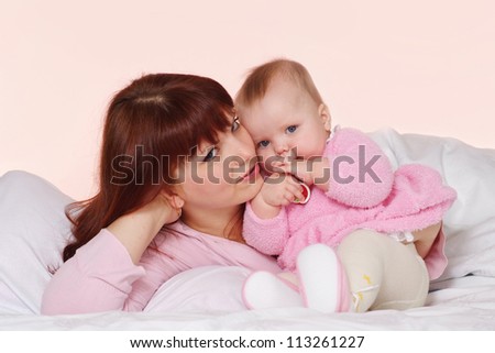 A Caucasian mama with her daughter lying in bed on a light background