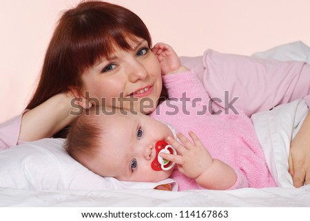 A happy Caucasian mummy with her daughter lying in bed on a light background