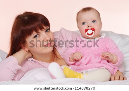 A beautiful good mama with her daughter lying in bed on a light background