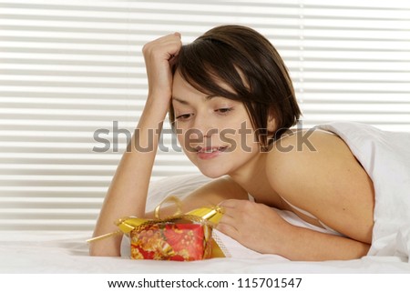 portrait of a beautiful woman lying with a gift on a white bed