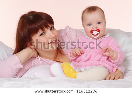 A beautiful happy mama with her daughter lying in bed on a light background