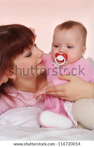 A beautiful Caucasian mummy with her daughter lying in bed on a light background