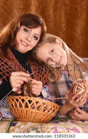 portrait of a nice mom and daughter knitting on a brown background