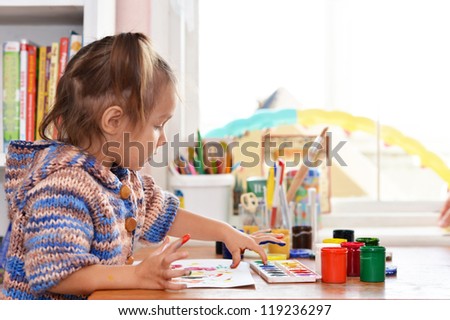 Portrait of a nice baby draws paints at the table