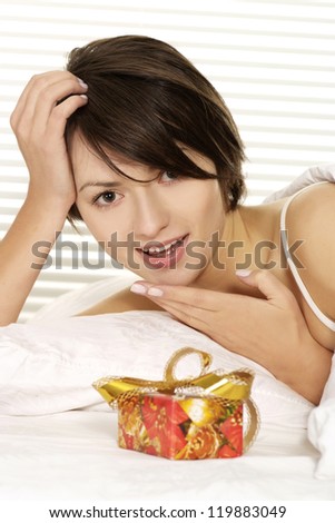 Portrait of a surprised young woman with a gift on a white bed