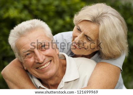 Beauteous elderly couple in the park on a background of green trees and bushes