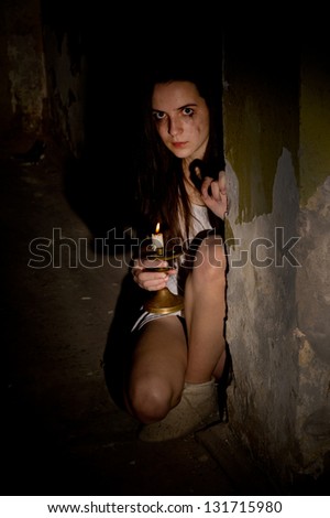 frightened young woman with a candlestick in a dark cellar