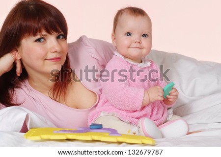 A beautiful pretty mother with her daughter lying in bed on a light background