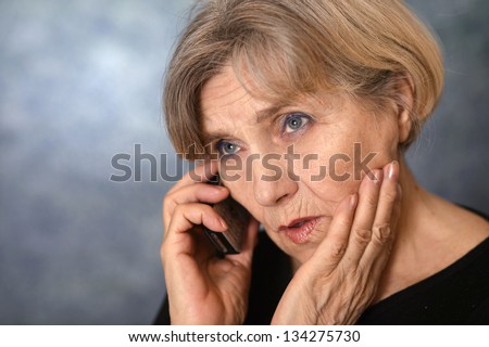 portrait of a sad old woman calling on a gray background
