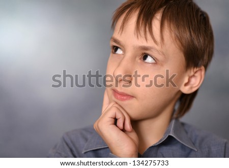 portrait of a thinking little boy over a gray background