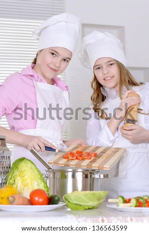 Two cheerful teen girls preparing dinner in the kitchen at home