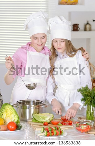 Two cheerful teen girls preparing dinner in the kitchen at home