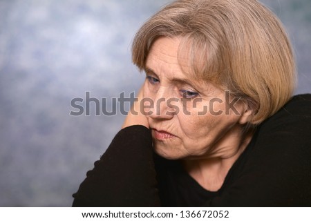 portrait of a sad older woman in a black sweater over gray background
