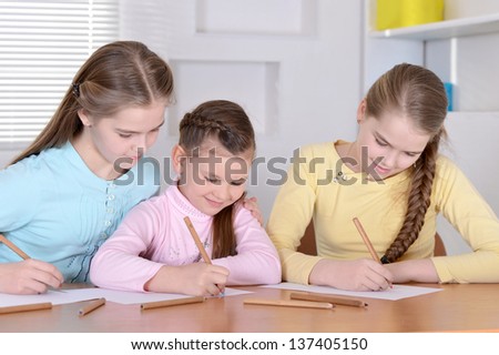 three young girls  draw with pencils  at the table at home