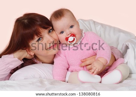 A beautiful good mummy with her daughter lying in bed on a light background