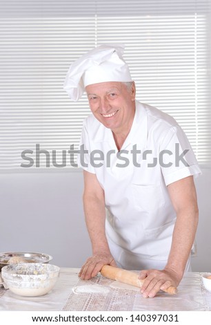elderly man in a cap chef knead the dough