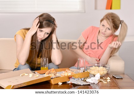 Two young girlfriends eat pizza at home
