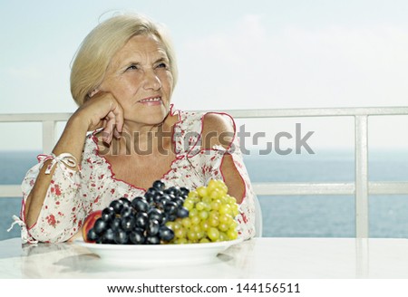 Happy elderly woman with a plate of grapes on the background of the sea in summer