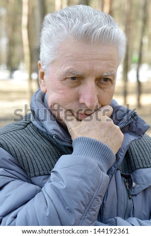 Pensive elderly man walking in the forest in autumn
