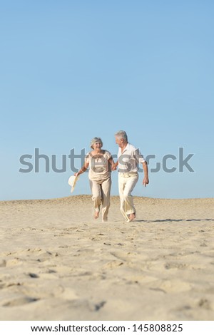 happy elderly couple walking barefoot on the sand in the summer