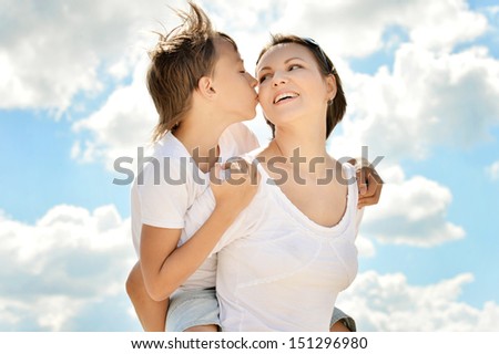 Son kissing his mother on background of a sky