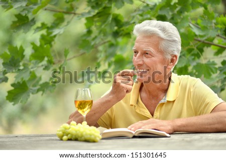 Old man sitting at a table, drinking wine and reading a book