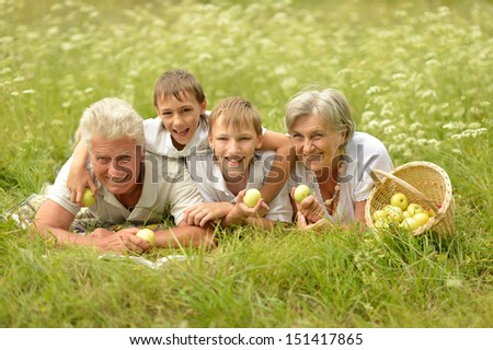 Older man and woman with their grandchildren resting on green grass
