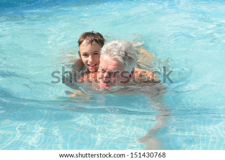 Grandfather swimming with grandson in a blue pool