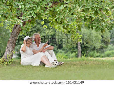Aged couple is sitting under a tree in green summer park
