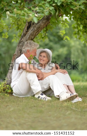 Aged couple is sitting under a tree in green summer park
