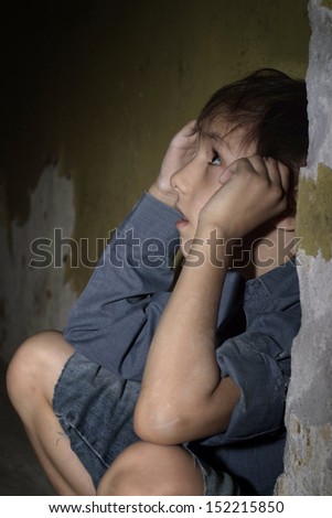 Scared lonely little boy in a dark cellar