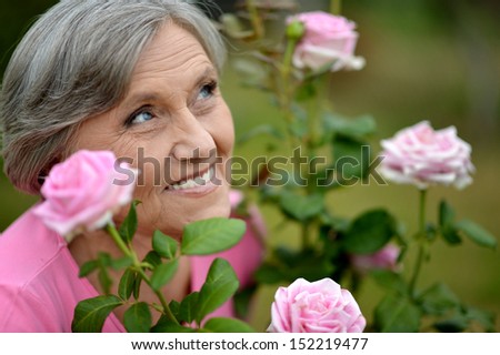 Happy elderly woman enjoying beautiful pink roses outdoors