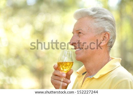 Smiling old man drinking wine in summer park