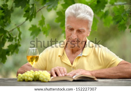 Old man sitting at a table, drinking wine and reading a book