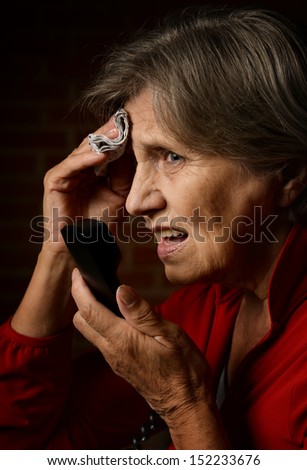 Older sick woman in red is speaking on phone on a dark background