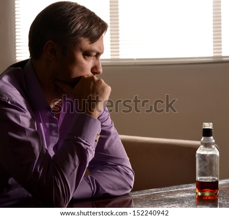 Cute and sad young man drinks whiskey at table